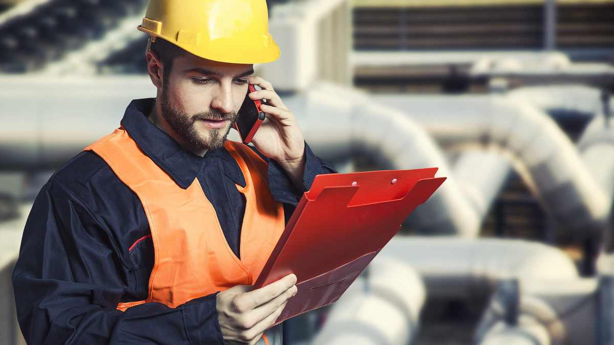 Man in high vis jacket and yellow building helmet holding a clipboard